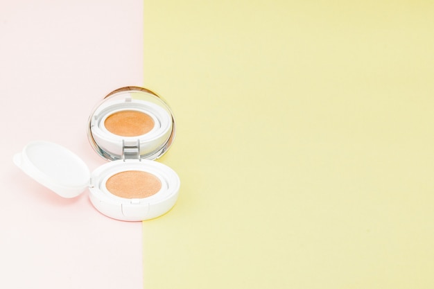 Make up prodotti che si rovesciano su uno sfondo giallo e rosa brillante con spazio di copia