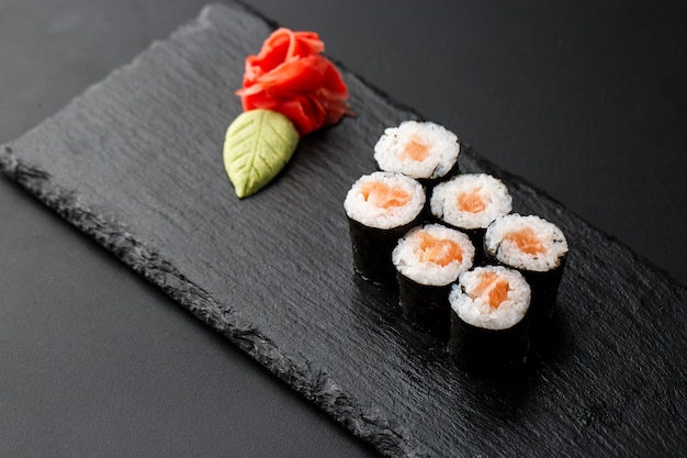 Maki Sushi Rolls con i salmoni sulla pietra nera su oscurità