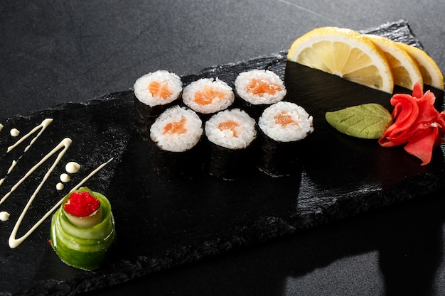 Maki Sushi Rolls con i salmoni sulla pietra nera su oscurità