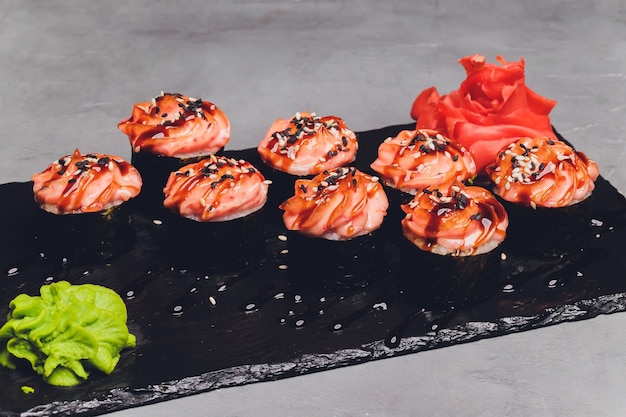 Maki Sushi Rolls con salmone su pietra nera su sfondo scuro. Con zenzero e wasabi. Menu di sushi. Cibo giapponese. Primo piano di delizioso cibo giapponese con rotolo di sushi. Foto orizzontale.