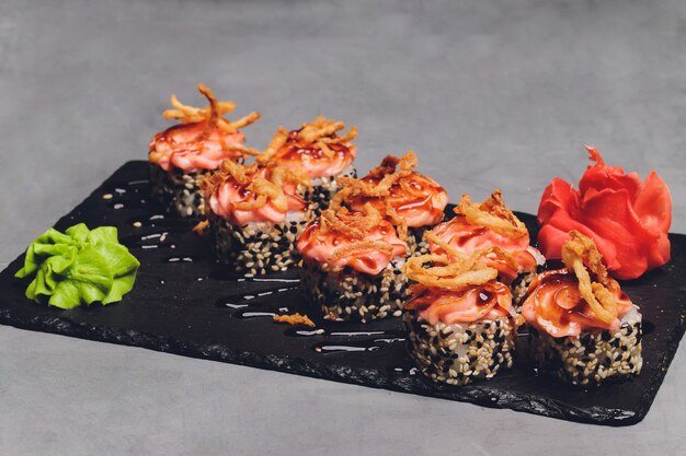 Maki Sushi Rolls con salmone su pietra nera su sfondo scuro. Con zenzero e wasabi. Menu di sushi. Cibo giapponese. Primo piano di delizioso cibo giapponese con rotolo di sushi. Foto orizzontale.