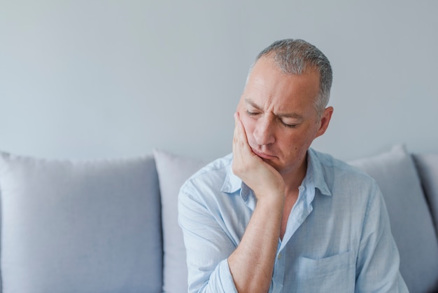 Mal di denti. Frustrato giovane che tocca la sua guancia e mantenendo gli occhi chiusi