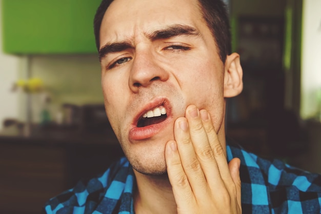 Mal di denti - giovane sofferente con problemi ai denti. Il ragazzo tiene la mascella del paziente era mano rotta. colpo alla mascella.