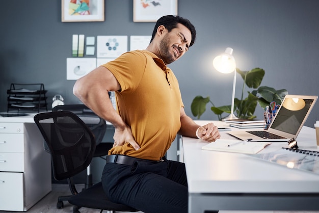 Mal di schiena uomo d'affari e stress di notte alla scrivania dell'ufficio con lesioni e problemi di salute Imprenditore maschio asiatico con tecnologia salute mentale o esaurimento mentre è stanco o affaticato e lavora fino a tardi