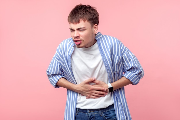 Mal di stomaco Ritratto di uomo malato dai capelli castani con piccola barba e baffi in camicia casual che tocca la pancia soffre di dolore addominale gastrite o stitichezza indoor isolato su sfondo rosa