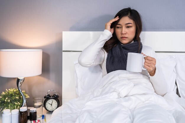 Mal di testa della donna malata e bere una tazza di acqua calda sul letto