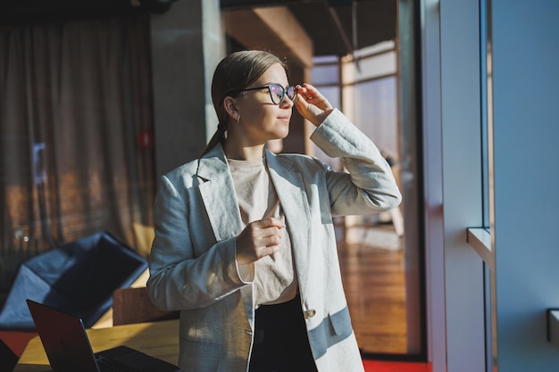 Mal di testa nella giovane donna d'affari in abiti casual e occhiali in ufficio Emicrania dal lavoro d'ufficio