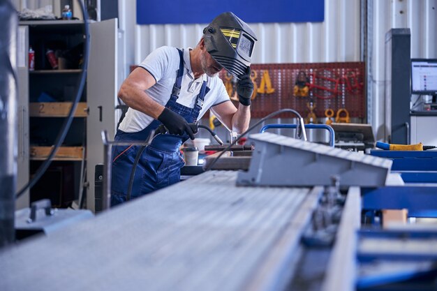 male worker in gloves taking off protective mask while holding welding torch