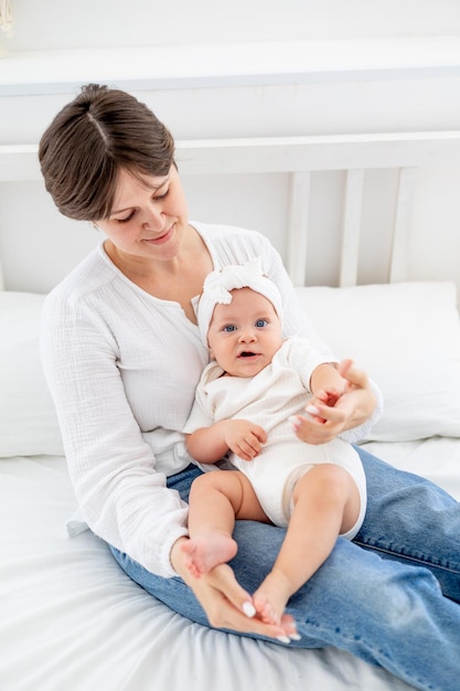 mamma abbraccia dolcemente la sua bambina baciandola e ammirandola famiglia felice mamma con bambino sul letto amore e cura materni mamma in congedo di maternità che gioca con il bambino