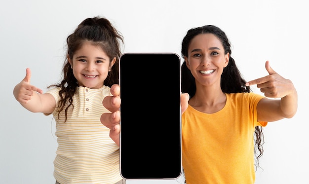 Mamma araba e figlia carina che puntano allo smartphone con schermo nero
