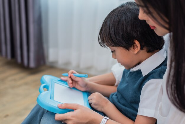 Mamma asiatica che insegna al ragazzo sveglio a assorbire lavagna insieme. Ritorno a scuola e Educatio