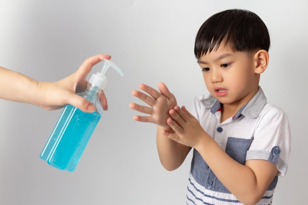 Mamma asiatica che usando il gel antisettico dell'alcool per le mani di pulizia del bambino. Disinfezione da coronavirus