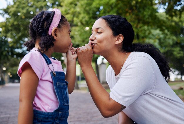 Mamma bambino e divertente giocare al parco insieme con le mani alla bocca in un gesto di bacio carino sul sentiero del giardino Ama la felicità e la madre e la bambina hanno tempo per legare con giochi all'aperto e sviluppo felice