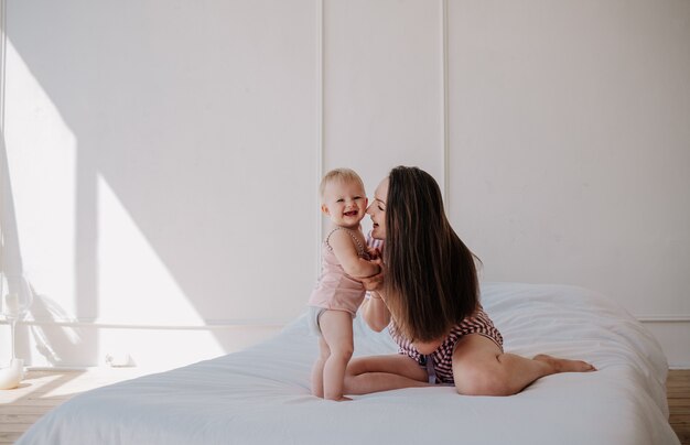 Mamma bruna in pigiama seduta sul letto con una bambina in camera da letto