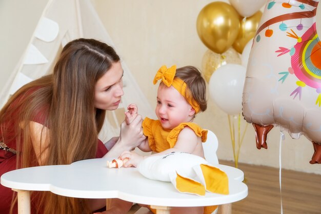 Mamma caucasica lenisce e bacia una figlia di un anno che piange, foto in studio per un bambino di un anno