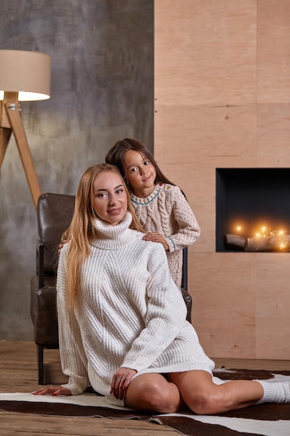 Mamma con bambina che si rilassa sul pavimento vicino a un accogliente divano luci di Natale nel camino