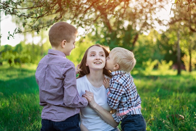 Mamma con due figli nel parco. Il bambino sta baciando sua madre. Felice maternità