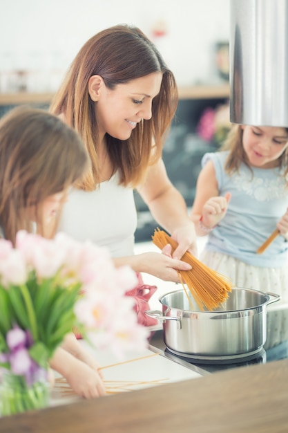 Mamma con due giovani figlie gemelle in cucina che cucinano gli spaghetti.