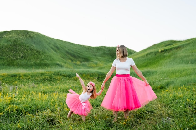 Mamma con figlia in abiti rosa che camminano nel campo Madre con figlia con gli stessi vestiti Famiglia stesso look Stile di moda Abbigliamento per genitori e figli Vacanze in famiglia insieme nella natura
