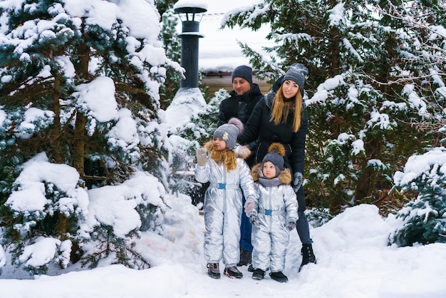 Mamma con papà e figlio e figlia in inverno nel cortile vicino al fiocco di neve cadente dell'albero di Natale innevato...