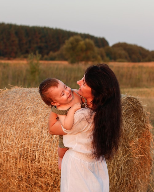 Mamma con un bambino in braccio in un campo al tramonto Concetto di famiglia felice e di vacanze estive