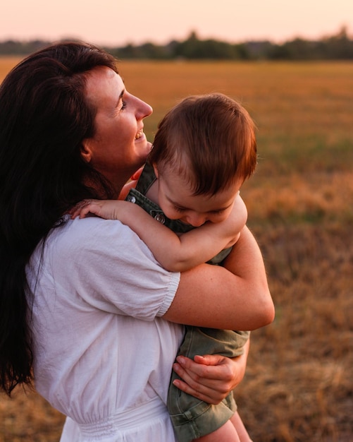 Mamma con un bambino in braccio in un campo al tramonto Concetto di famiglia felice e di vacanze estive