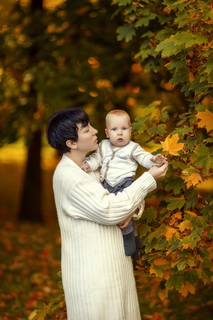 Mamma con un maglione leggero con un bambino in braccio sullo sfondo dell'autunno dorato