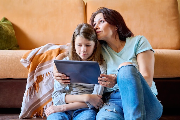 Mamma di mezza età e figlia preteen che si rilassano a casa insieme alla tavoletta digitale