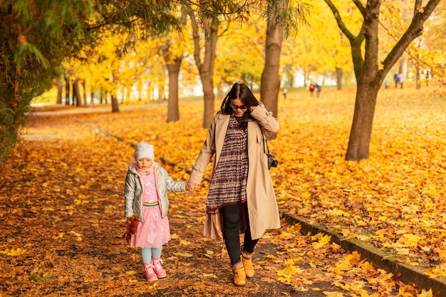 Mamma donna con figlia che cammina nel parco autunnale con fogliame giallo