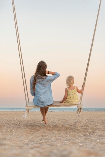 Mamma e bambina si siedono sull'altalena e guardano lo splendido tramonto sul mare Alba magica sul mare