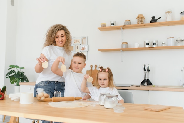 Mamma e bambini felici che mescolano gli ingredienti per la pasta fatta in casa della torta, della torta o del biscotto in cucina.