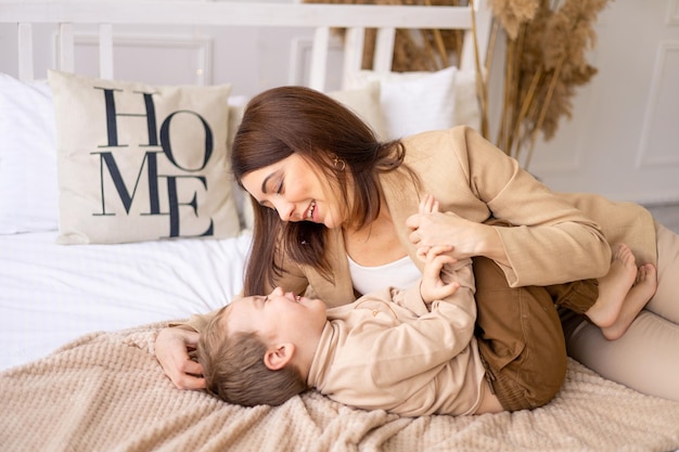 Mamma e bambino giocano a coccolarsi e scherzare a casa su un letto nei toni del marrone naturale una famiglia felice con un bambino piccolo si diverte insieme