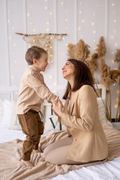 Mamma e bambino giocano a coccolarsi e scherzare a casa su un letto nei toni del marrone naturale una famiglia felice con un bambino piccolo si diverte insieme