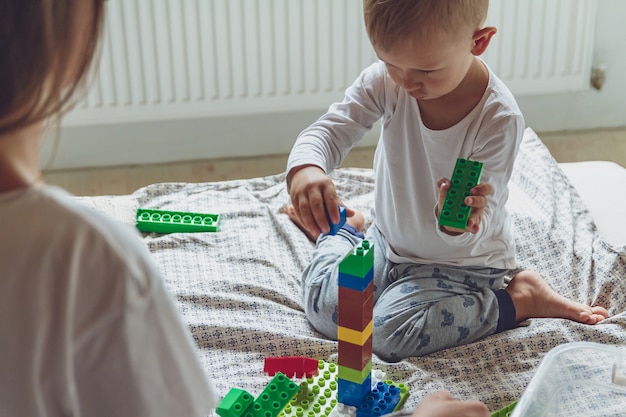 Mamma e bambino giocano insieme in camera da letto su un letto con blocchi di plastica