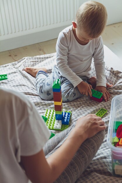 Mamma e bambino giocano insieme in camera da letto su un letto con blocchi di plastica