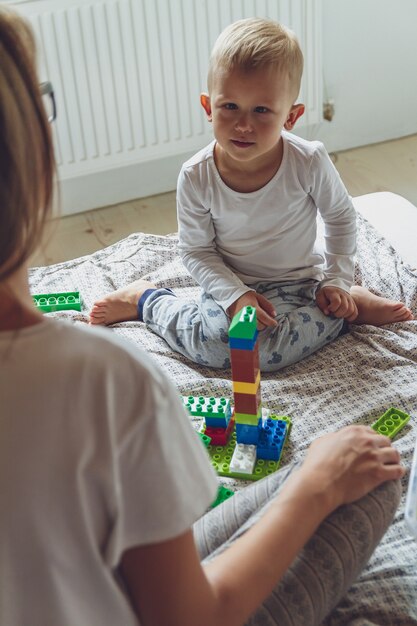 Mamma e bambino giocano insieme in camera da letto su un letto con blocchi di plastica