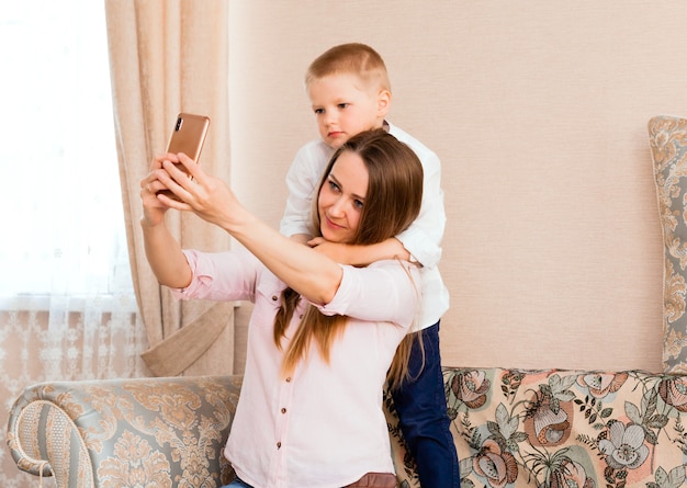 Mamma e bambino si fanno un selfie in un accogliente soggiorno. mamma e figlio fanno facce buffe e si fotografano davanti alla telecamera