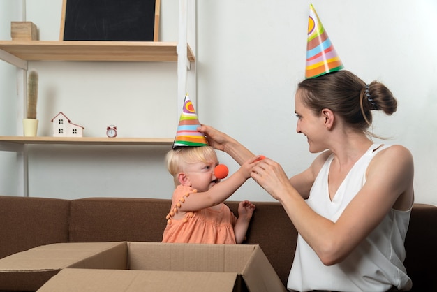 Mamma e bambino si stanno preparando per le vacanze. Cappello da festa e naso da clown per la piccola figlia.