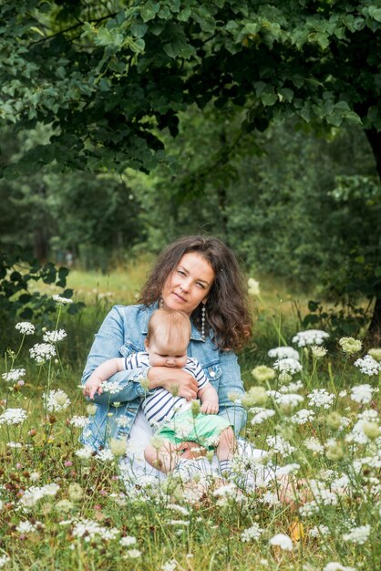 Mamma e bambino sono seduti in un parco sotto un albero tra i fiori e sorridono.Campo di fiori, picnic all'aperto.