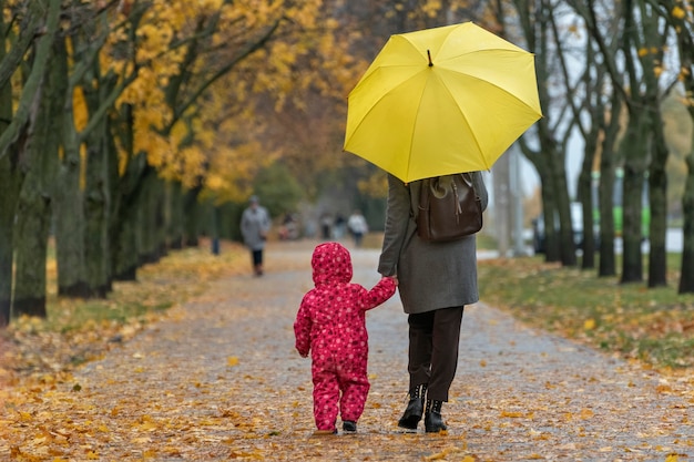 Mamma e bambino stanno camminando sotto l'ombrellone lungo il vicolo del parco autunnale. Vista posteriore