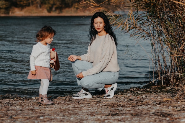 Mamma e bambino sulla spiaggia sullo sfondo di un lago blu, mamma gioca con sua figlia sul lago. natura autunnale