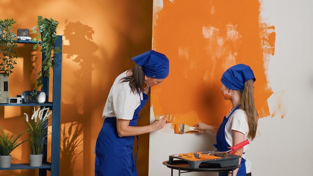 Mamma e bambino usano la vernice arancione per rinnovare le pareti della stanza e l'interno dell'appartamento, dipingendo lo spazio con colori e pennello. Migliorare i lavori domestici insieme a strumenti fai-da-te. Scatto da treppiede.