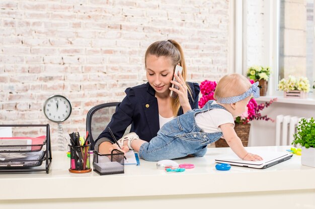 Mamma e donna d'affari che lavorano con il computer portatile a casa e giocano con la sua bambina.