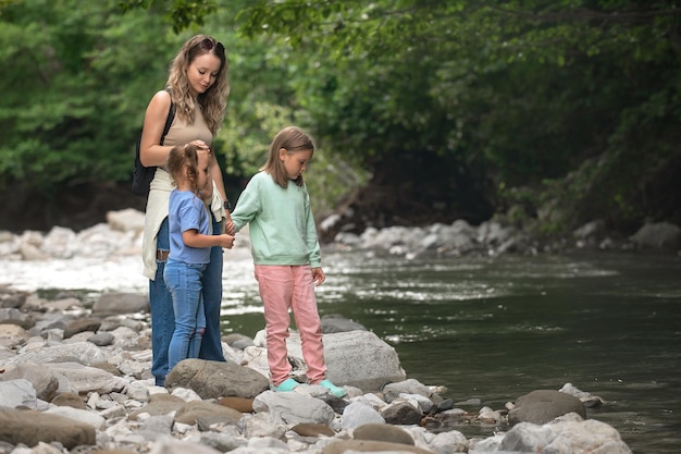 mamma e due figlie piccole stanno facendo un'escursione vicino a un fiume di montagna con una corrente.