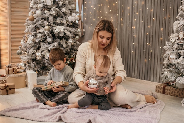 Mamma e figli sono seduti per terra in una stanza con un albero di Natale