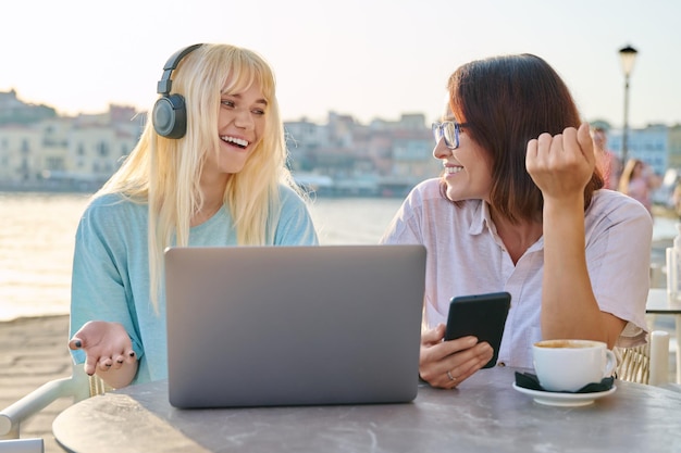 Mamma e figlia adolescente guardando il computer portatile insieme seduti in un caffè all'aperto