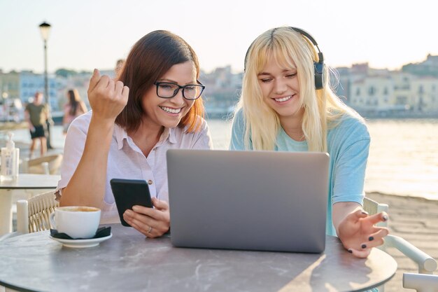 Mamma e figlia adolescente guardando il computer portatile insieme seduti in un caffè all'aperto