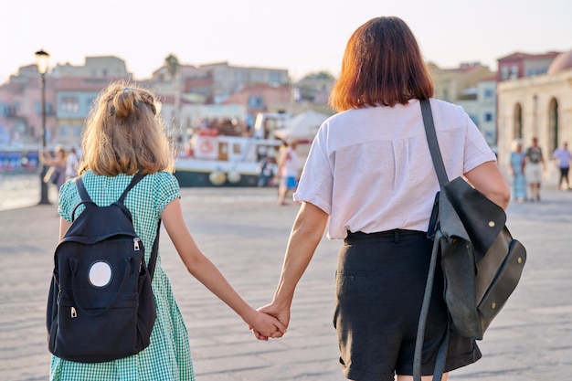 Mamma e figlia bambino con zaino che si tengono per mano insieme vista posteriore