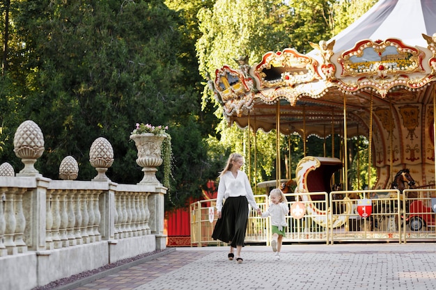 Mamma e figlia camminano nel parco la sera d'estate e sorridono