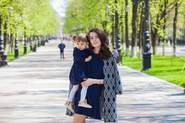 Mamma e figlia con gli stessi vestiti per una passeggiata nel parco. Figlia tra le braccia di mamma. La tenerezza della maternità